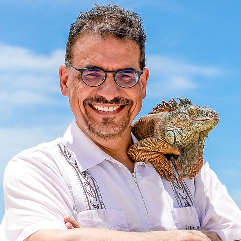 man with glasses smiles and has a lizard perched on his shoulder
